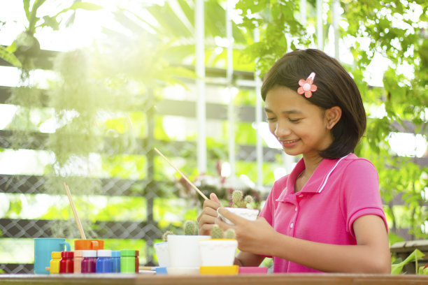 快乐的亚洲小女孩在绿色自然背景的仙人掌壶上画颜色。图片下载