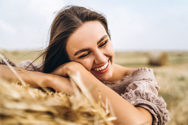 闭着眼睛微笑的美丽女人的特写。黑发女人靠在一捆干草上。背景是一片麦田图片下载