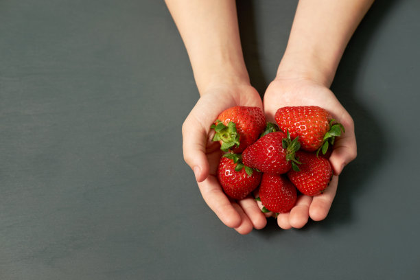 灰色的背景上，孩子手里拿着成熟的草莓。副本的空间。图片下载