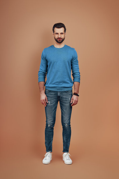 全长英俊的年轻人在休闲穿看着相机，而站在棕色的背景图片下载