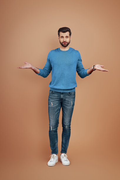 这名快乐的年轻人全身伸展着双臂，站在棕色背景下看着镜头图片下载