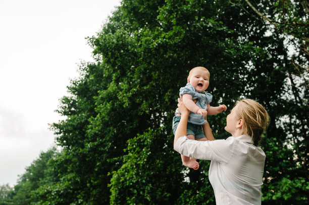 母亲把婴儿扔进大自然，女孩在天空中飞翔。拍摄妈妈和孩子在一起的照片。妈妈，小女儿在外面。年轻的妈妈带着小女孩在公园散步。家庭在花园度假。图片下载
