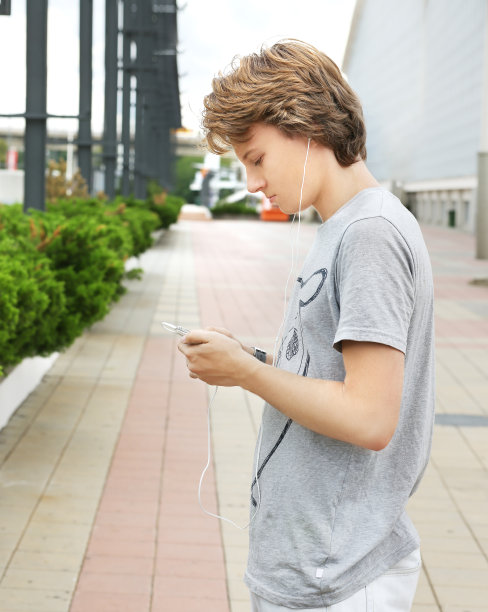 都市背景的迷人少年。十几岁的男孩在户外听音乐发短信图片下载