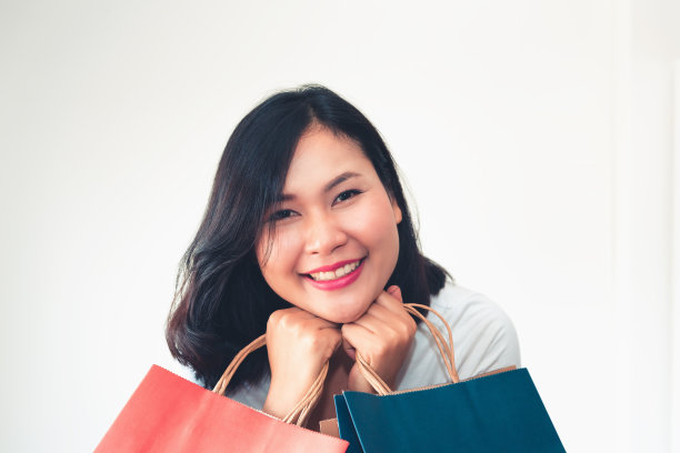 穿着白色t恤和牛仔裤的女人在明亮的白色背景前拿着许多购物袋图片下载