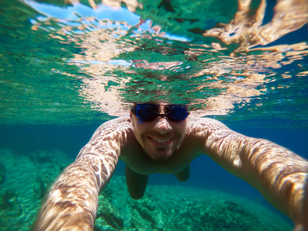 水下的观点，一个年轻的潜水员在绿松石海下游泳与浮潜面具的夏季假期，同时与一根棍子自拍。图片下载