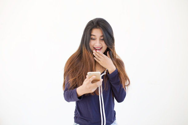 在白色背景上用智能手机微笑的女商人。肖像惊讶的年轻女孩看手机看到新闻或照片与有趣的情绪。图片下载