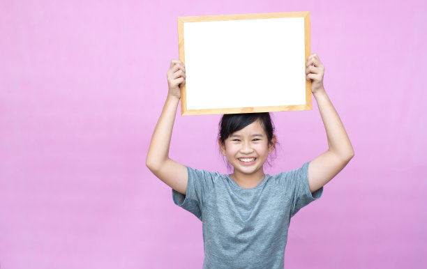 亚洲小女孩拿着白板，粉红色背景上的孤立。图片下载