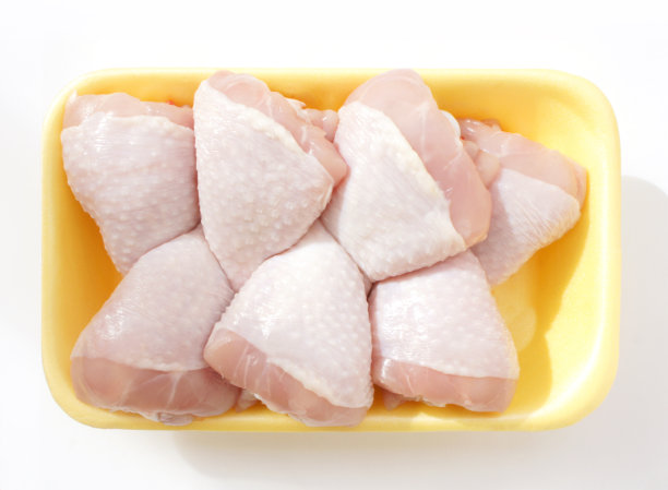 鸡腿装在黄色的聚苯乙烯容器里。一套七个生鸡腿烹饪在光的背景。前视图。图片下载