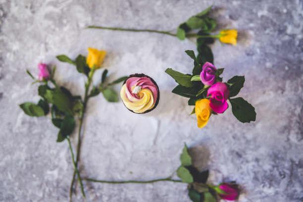 粉红色和黄色的纸杯蛋糕配上紫红色和黄色的玫瑰花图片下载