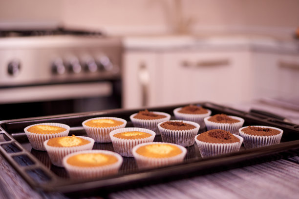 在厨房背景的桌子上，烤盘上放着纸杯蛋糕。图片下载