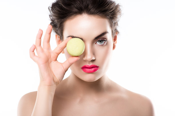 年轻时尚的女人捧着绿色的马卡龙在眼前，孤立在白色之上图片下载