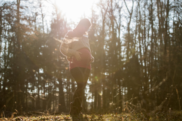 一个年轻的孕妇站在秋天的森林里图片下载