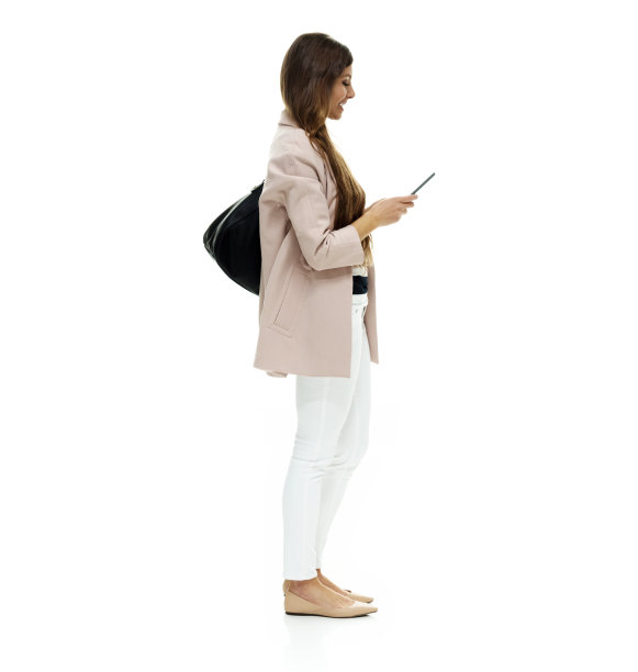 白人女性站在白色背景前，穿着外套，拿着钱包和使用智能手机图片下载