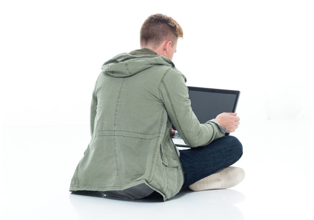 白人年轻男性坐在地板上，穿着衬衫，在白色的背景和使用电脑图片下载