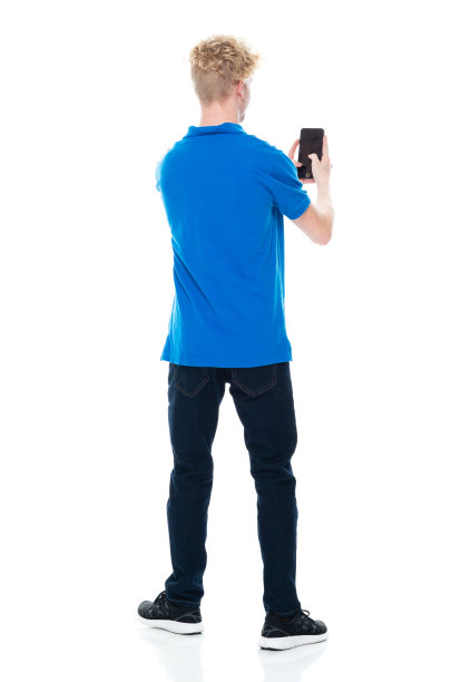 白人年轻男性穿着牛仔裤站在白色背景前，使用智能手机图片下载