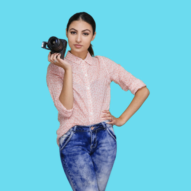 拉丁美洲和西班牙裔的年轻女性站在蓝色背景，穿着裤子，拿着相机图片下载