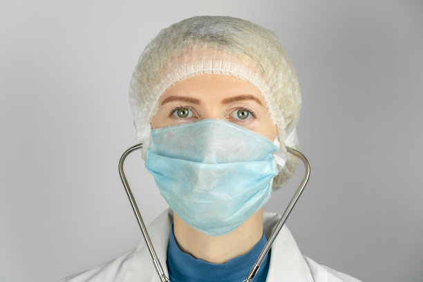 女孩穿着医疗袍，戴着医用口罩和医用帽，耳朵上插着听诊器，背景很亮。医学概念，实习生图片下载