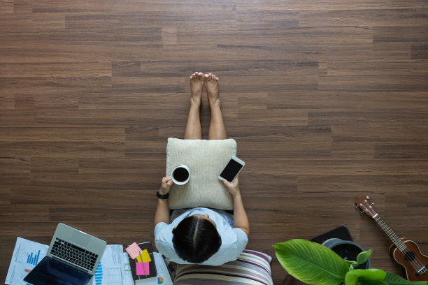 顶视图女人放松使用智能手机和喝咖啡在木地板上，在家工作的想法概念图片下载