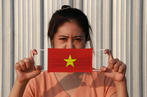 一名手持越南国旗卫生口罩的妇女在灰色背景下抬起了正面的脸。微粒或病毒冠状或Covid - 19的保护。图片下载