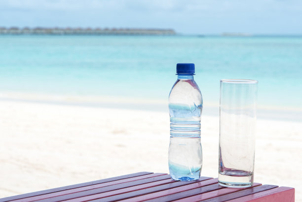沙滩桌上有一瓶矿泉水和一个玻璃杯图片下载