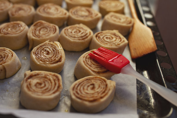 在黑色的烤盘上，用烤纸和红色的硅树脂刷自制肉桂面包素材图片