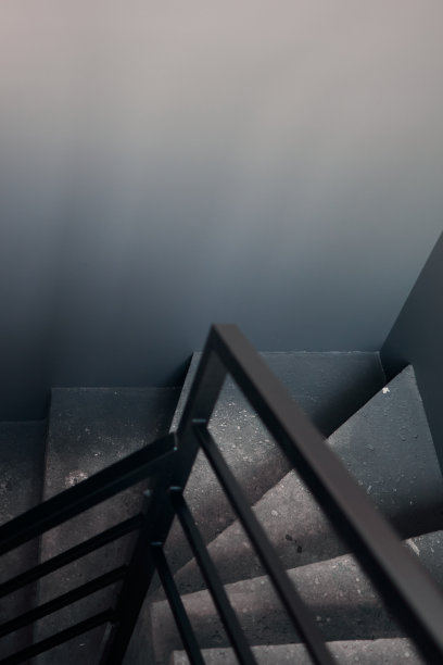 黑色石墙角落背景上的螺旋楼梯的特写。黑色大厅内部粗糙的混凝土楼梯与黑色钢扶手。简约的室内设计。图片下载