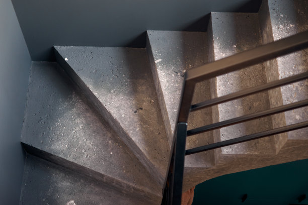 黑色石墙角落背景上的螺旋楼梯的特写。黑色大厅内部粗糙的混凝土楼梯与黑色钢扶手。简约的室内设计。图片下载