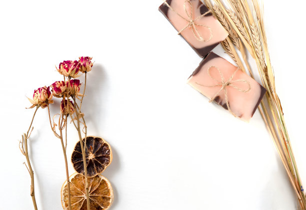 平面构图，两种带有橙色色调的手工制作的棕粉色肥皂，干燥的橘子片，玫瑰花和小麦穗，白色的背景和木质的纹理。水平的照片。手工化妆品的概念与自然图片下载