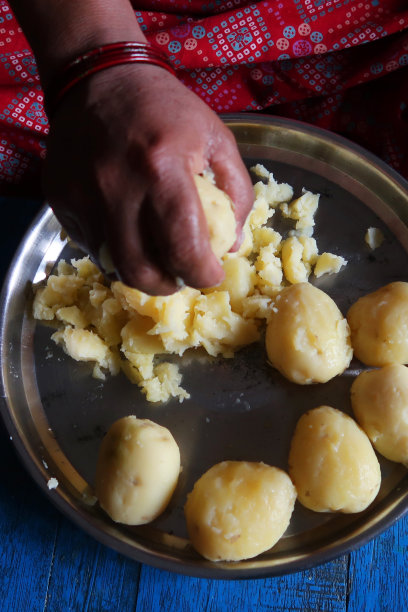 照片中，一位面目全非的亚洲妇女盘腿坐在地板上准备土豆泥，右手捏碎土豆泥图片下载