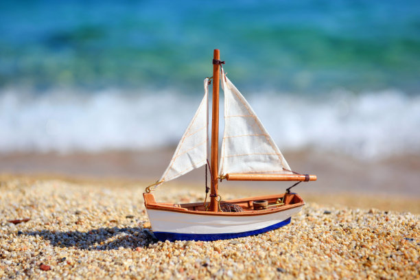 海滩上的迷你玩具帆船，以大海和海浪为背景。度假和旅行的概念。图片下载