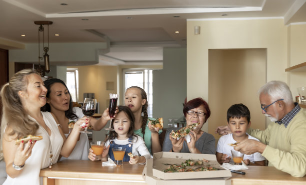 欢乐的家庭在厨房一起吃美味的披萨，用玻璃杯庆祝。图片下载