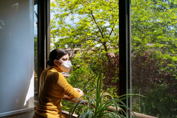 全景的女人看着透过窗户带着担心的表情戴着面具。图片下载