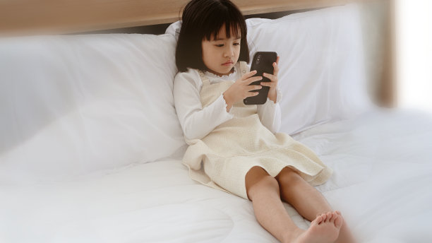 女孩在床上玩手机，社会问题导致儿童发育不足。图片下载