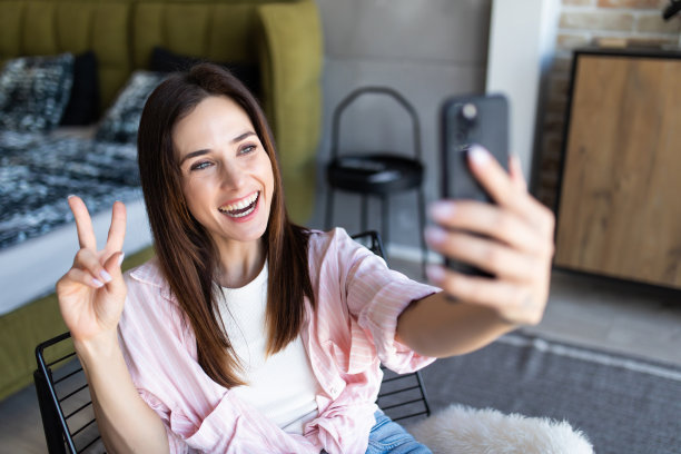 有魅力的女孩以和平的姿态拍自己的照片，坐在舒适的椅子在家里的客厅图片下载
