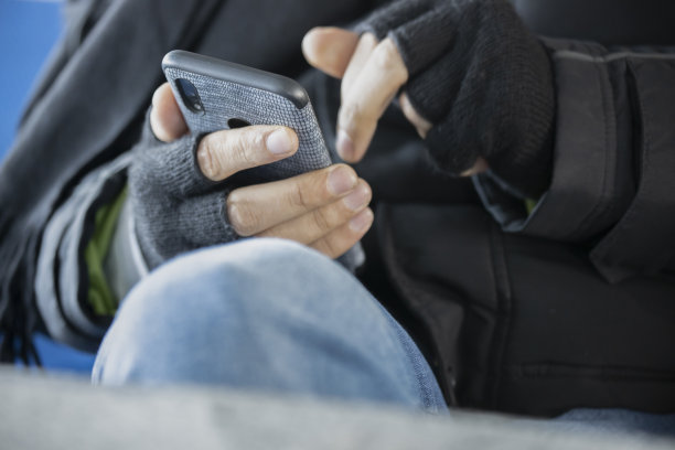 一名年轻人戴着无指手套照看他的智能手机。关闭了。图片下载