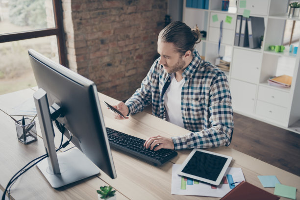 英俊的业务管理员男人照片电脑显示器桌子阅读电话客户客户回复穿休闲衬衫西装坐椅子现代室内办公室室内图片下载