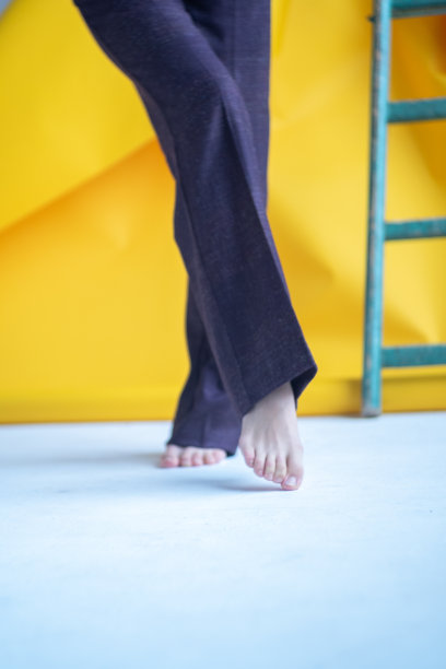 一名年轻女子在地板上赤脚走着，背景是一堵黄色的墙。图片下载