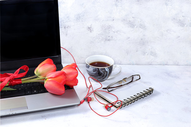 一个现代女性的桌面，家庭办公室。桌上放着电脑、一杯茶和春天的鲜花。简约的商业理念，家的舒适，图片下载