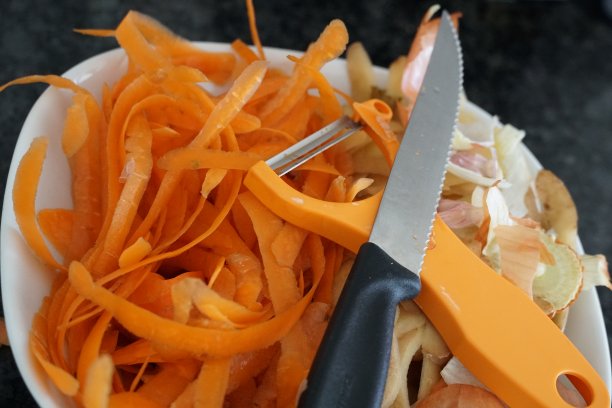 一个装有胡萝卜和洋葱皮的盘子，上面装有刀和削皮器，用来制作堆肥图片下载