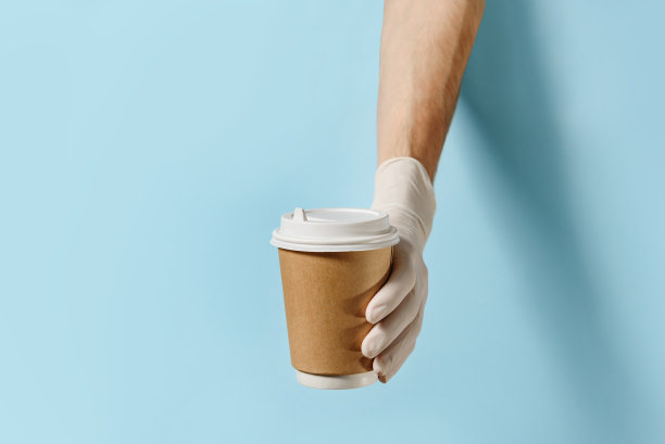 戴上防护手套，拿着纸杯在蓝色背景上放咖啡或茶图片下载