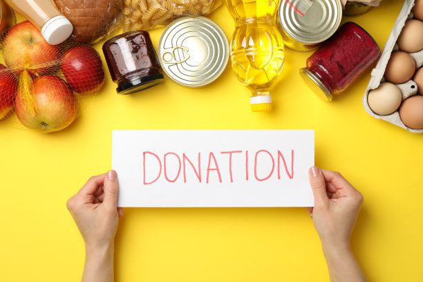 女性手握文字捐赠和不同的食物在黄色背景上，俯视图图片下载