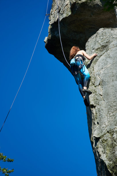 低角度观看一块巨大的岩石和一个女孩攀岩者，到达顶部图片下载