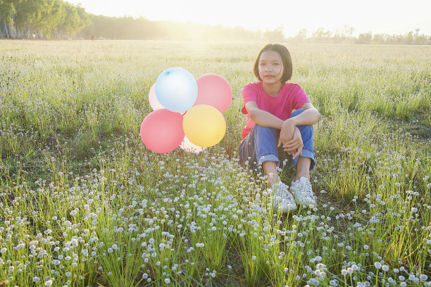 年轻的女孩坐着五颜六色的气球在草地上。图片下载