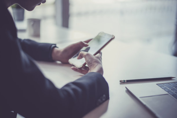 一名年轻女子坐在办公室里使用智能手机。图片下载