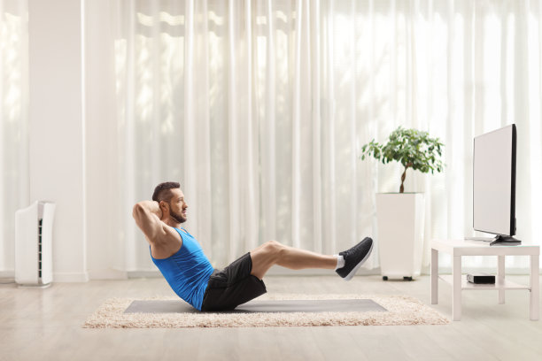 一个健康的年轻人在家看电视，在地板上锻炼腹肌图片下载