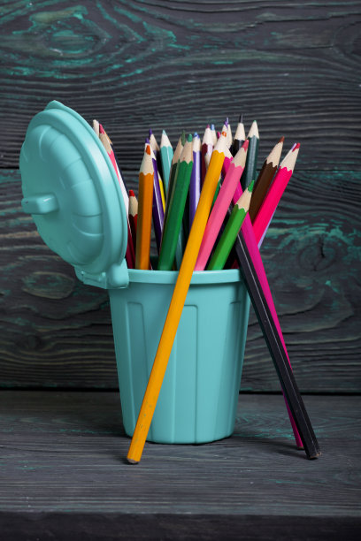 铅笔里装满了彩色铅笔。以垃圾容器的形式。在几支铅笔旁边。背景是刷成黑色和绿色的松木板。图片下载