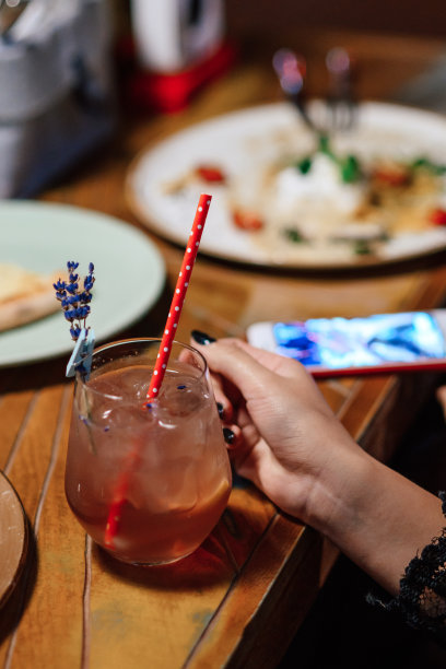 在一家餐馆的木桌背景上，女孩拿着一杯夏日清凉鸡尾酒。一只手的特写。用薰衣草枝装饰的鸡尾酒图片下载
