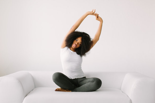 一位非裔美国年轻妇女在白色的床上以莲花坐姿坐着图片下载