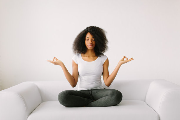 一位非裔美国年轻妇女在白色的床上以莲花坐姿坐着图片下载