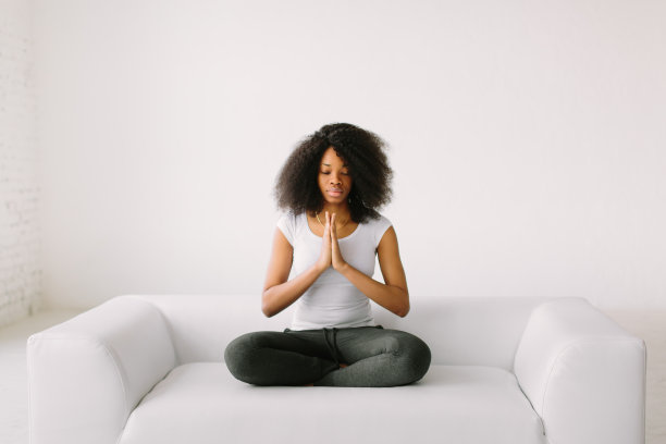 一位非裔美国年轻妇女在白色的床上以莲花坐姿坐着图片下载